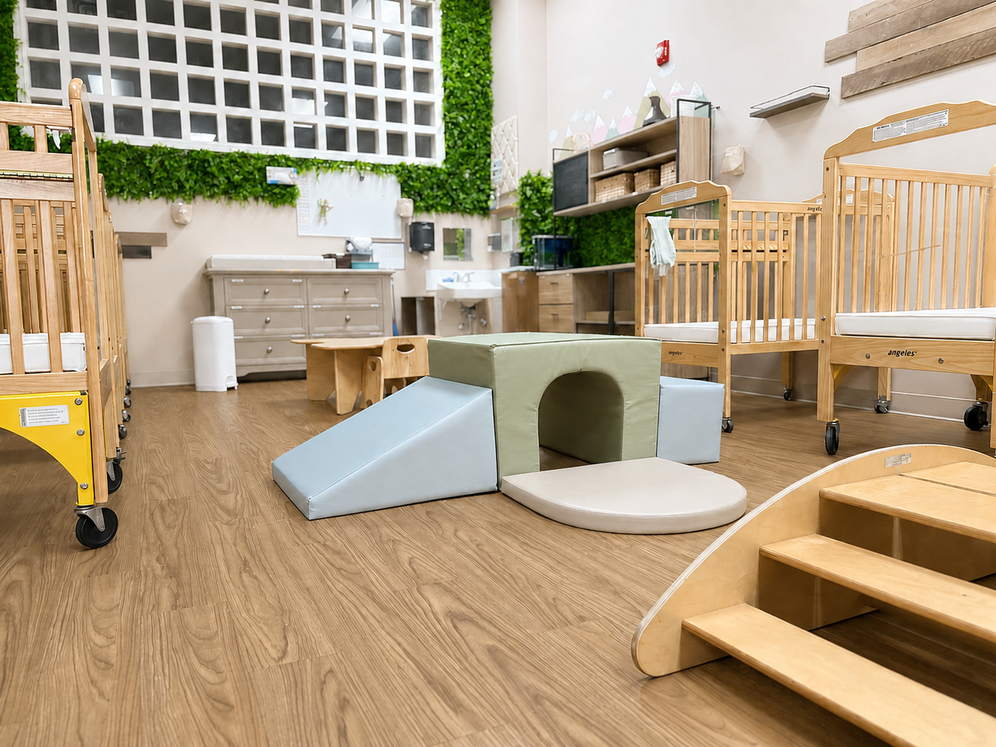 Lakeview's infant classroom with wooden cribs, climbing equipment, warm wood flooring, and greenery.