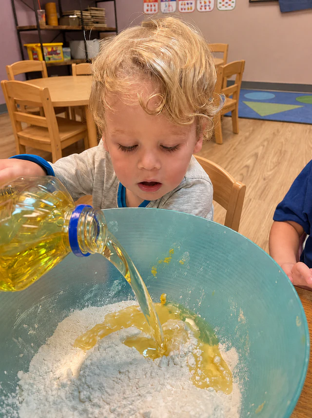 A child pouring liquid into a large mixing bowl during a classroom activity at L&L Lakeview.